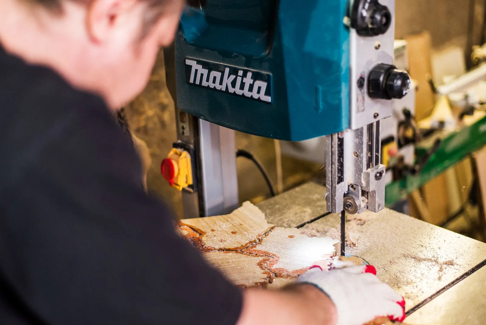 Close-up of a worker using a Makita band saw in a woodworking shop highlighting precision.